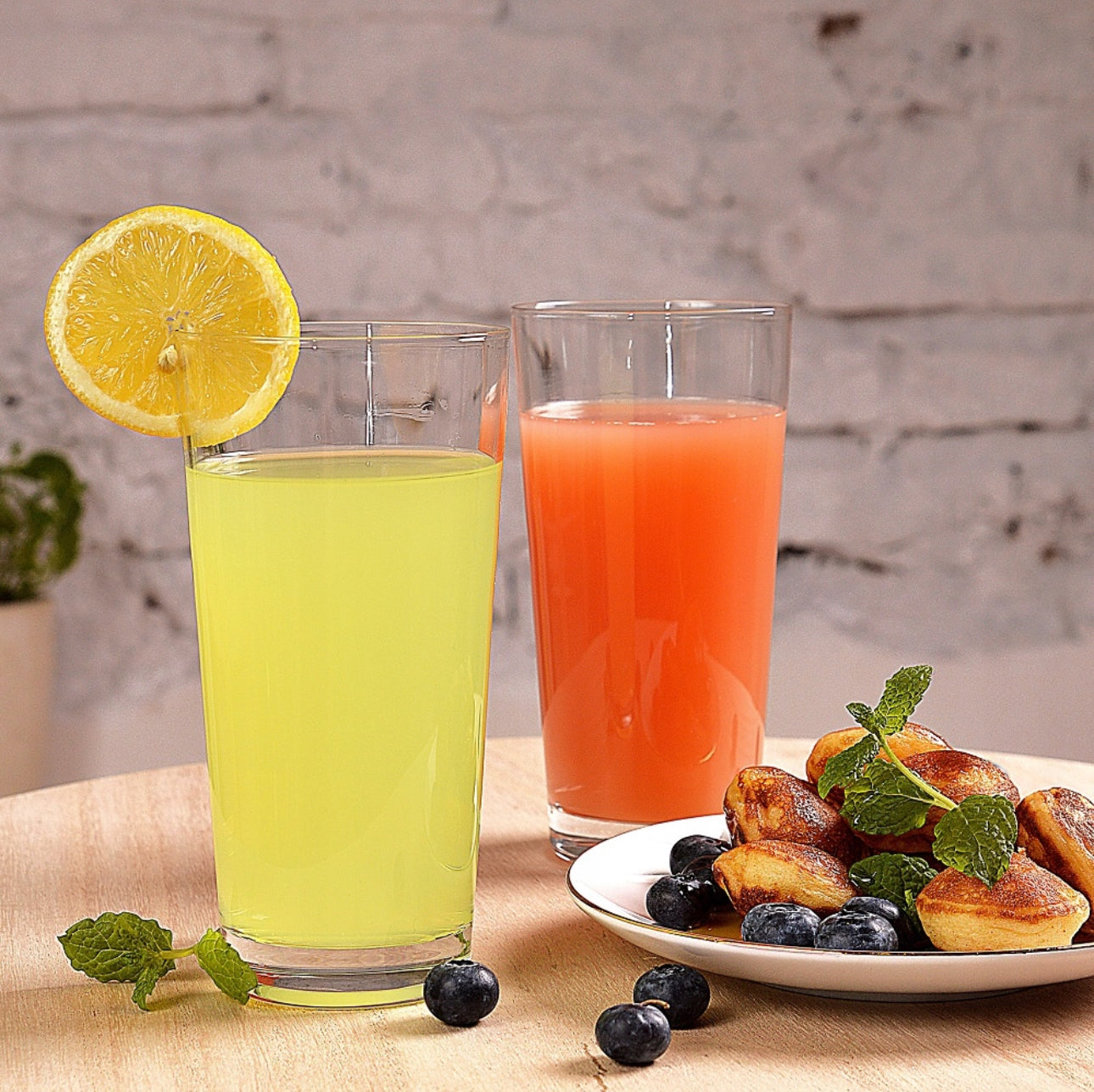 To glass med juice, sitron og små kaker på bord med friske blåbær