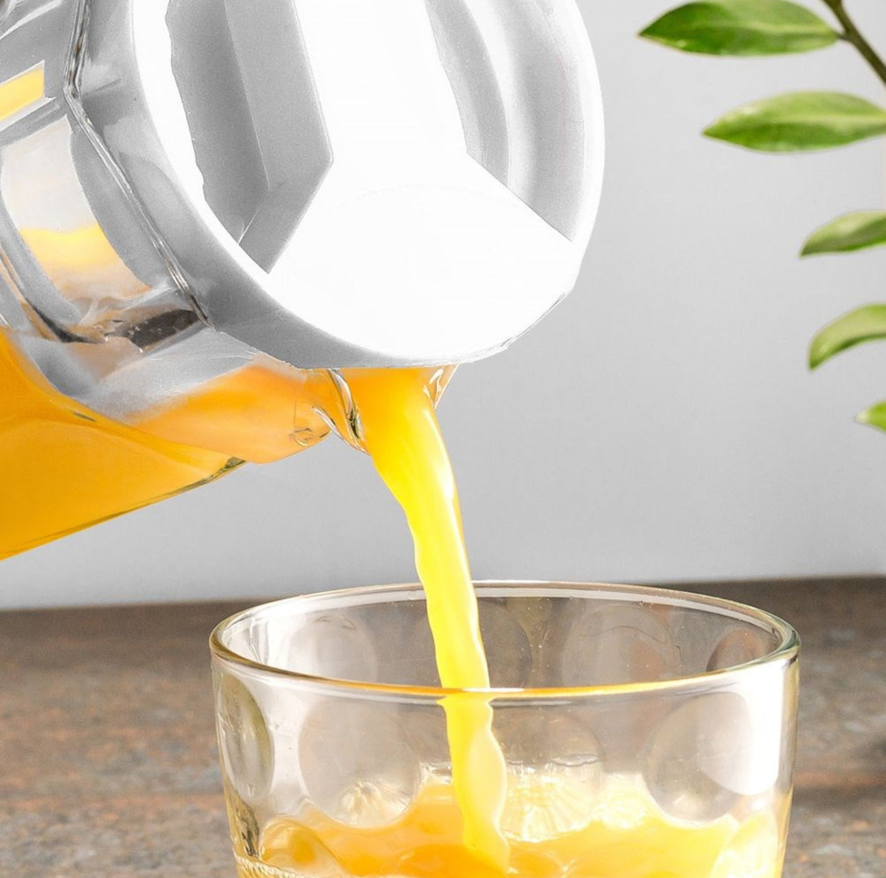 Nærbilde av juice som helles fra glasskanne i glass, moderne kjøkkenmiljø
