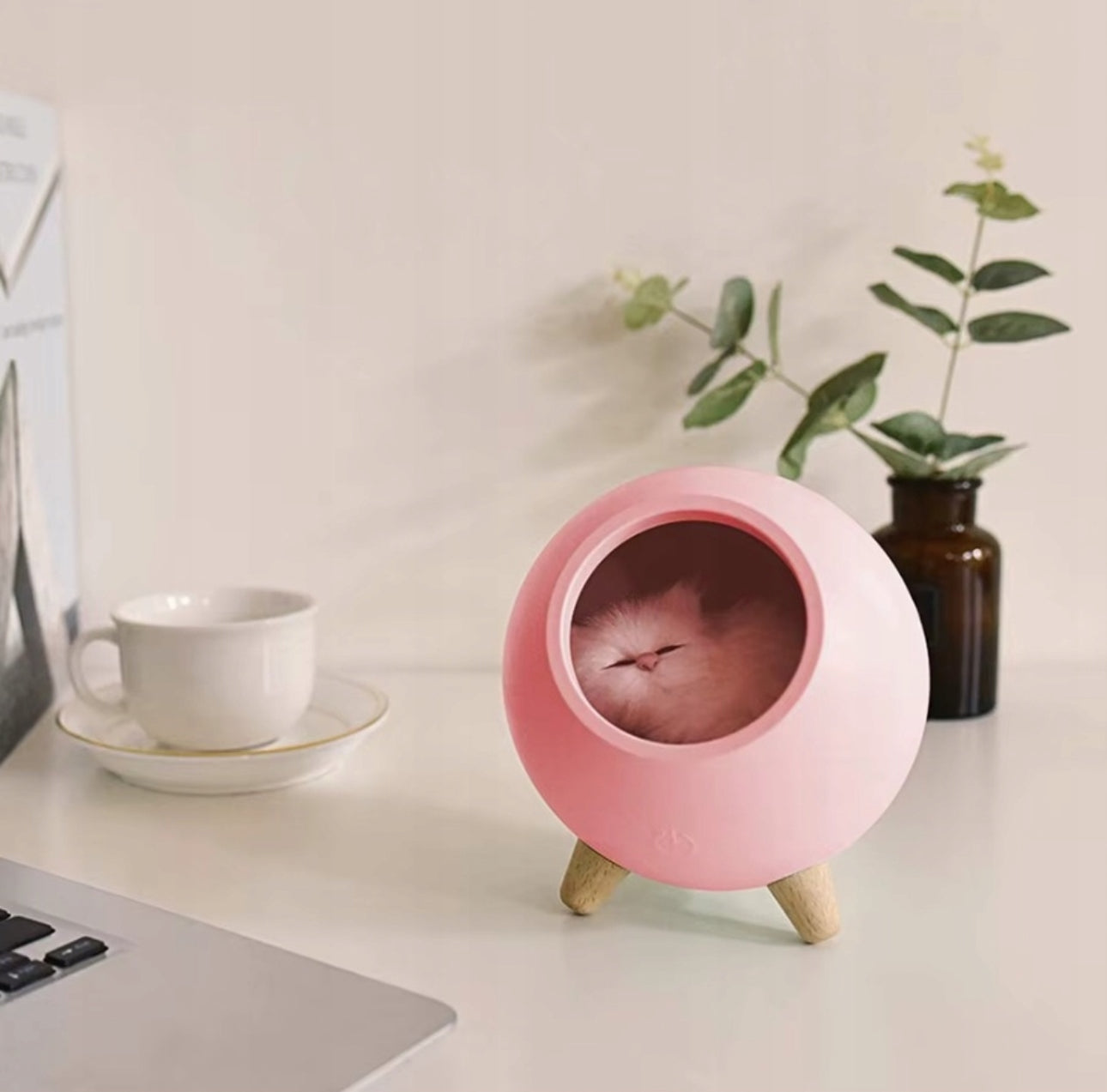 Rosa nattlampe med katt på hvit pult ved kopp og vase