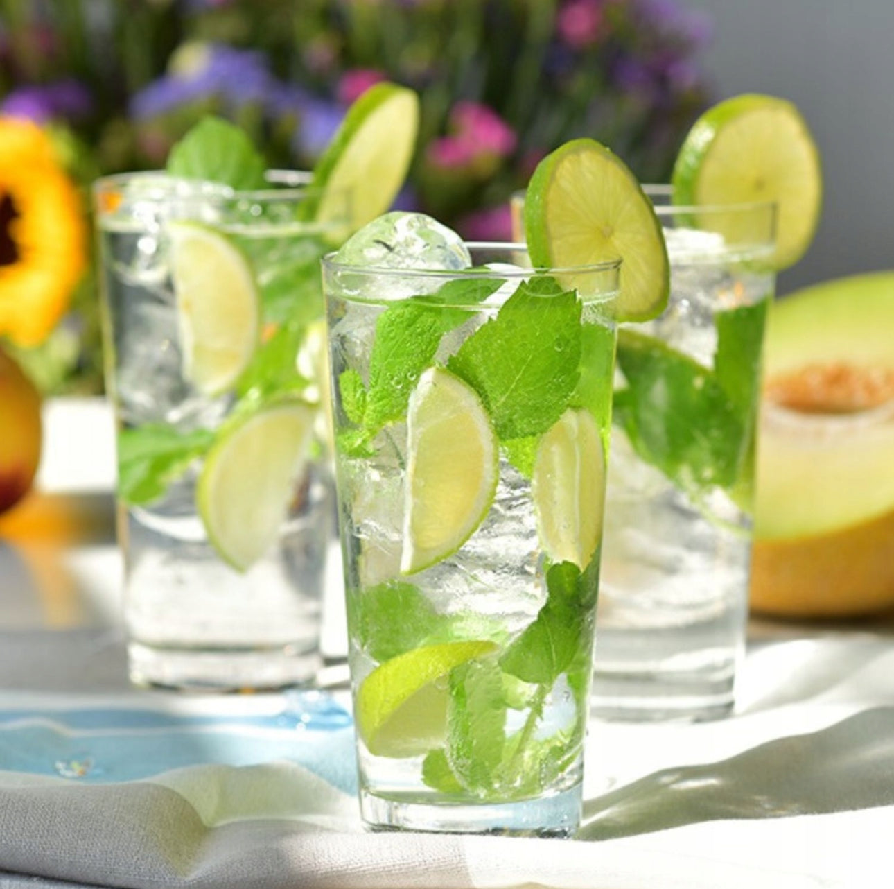 Tre høye glass med mojito, lime og mynte i solfylt utemiljø