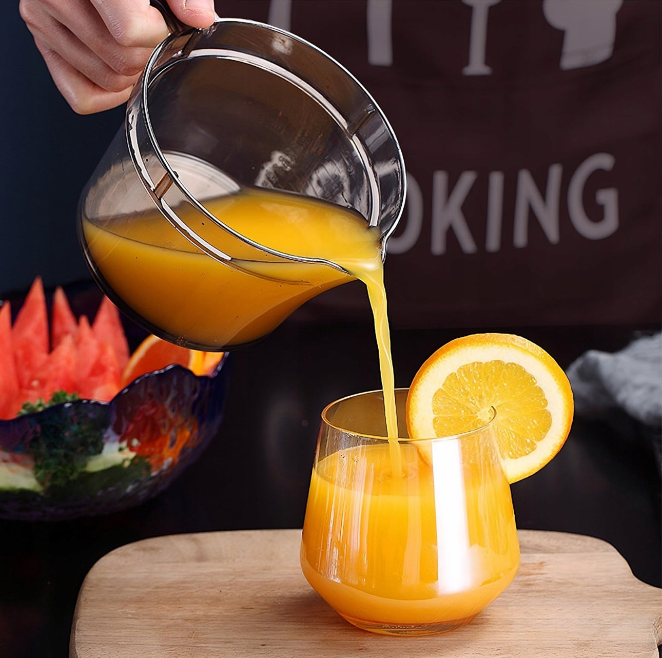 Sitruspresse heller fersk appelsinjuice i lavt glass med appelsinskive i kanten, frukt i bakgrunnen.