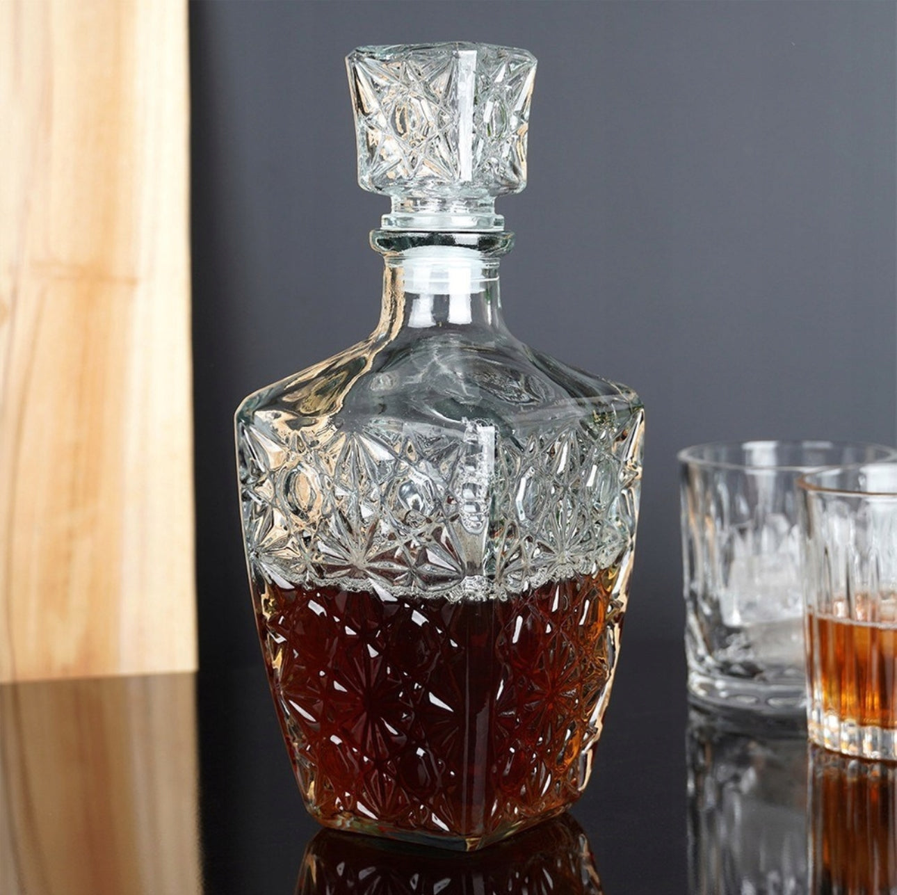 Glasskaraffel fylt med brun væske plassert på svart bord sammen med to whiskyglass