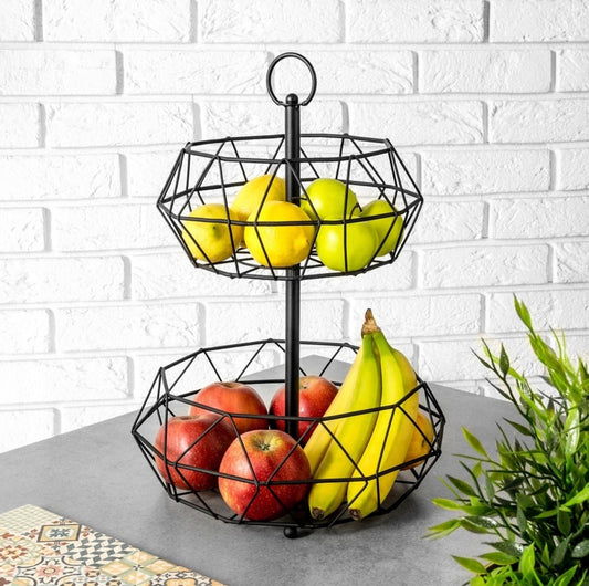 Tofatet metallkurv med svart geometrisk design fylt med frukt på grå benkeplate foran hvit murvegg