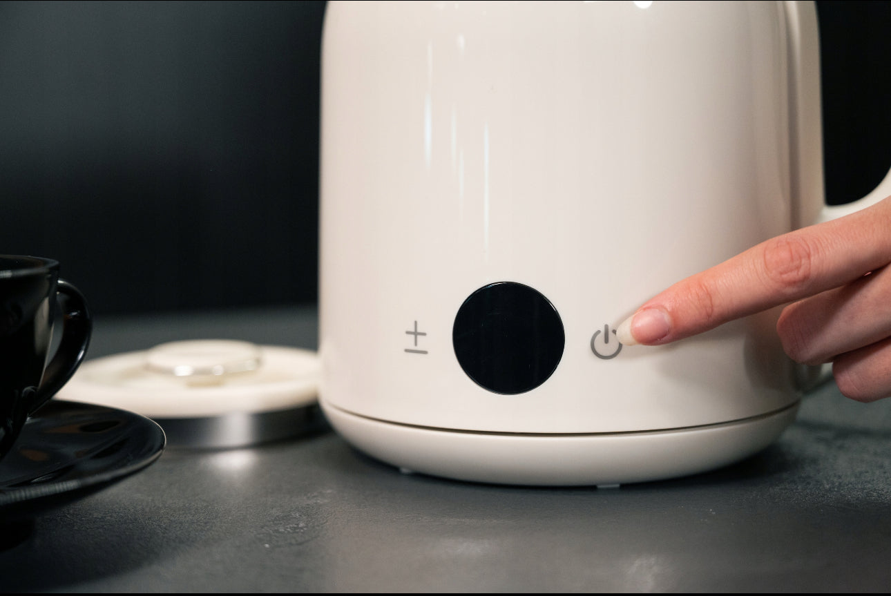 Finger trykker på på-knappen til vannkoker med minimalistisk digitalt kontrollpanel