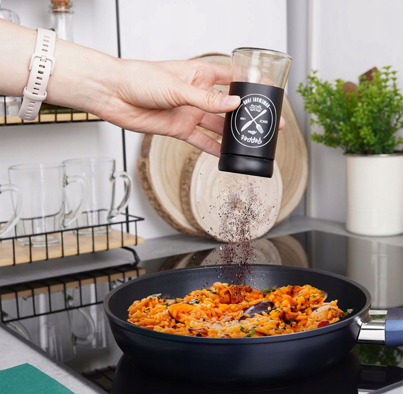 Hånd drysser pepper over pastarett med svart pepperbøsse i moderne kjøkken