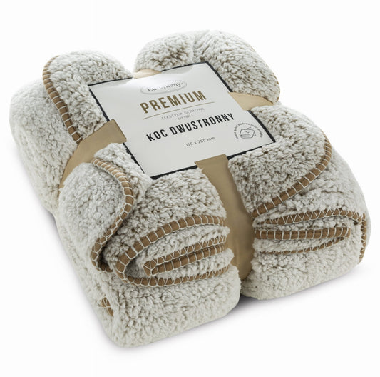 Sammenrullet bouclé-pledd i beige og hvitt med dekorativ kant og bånd
