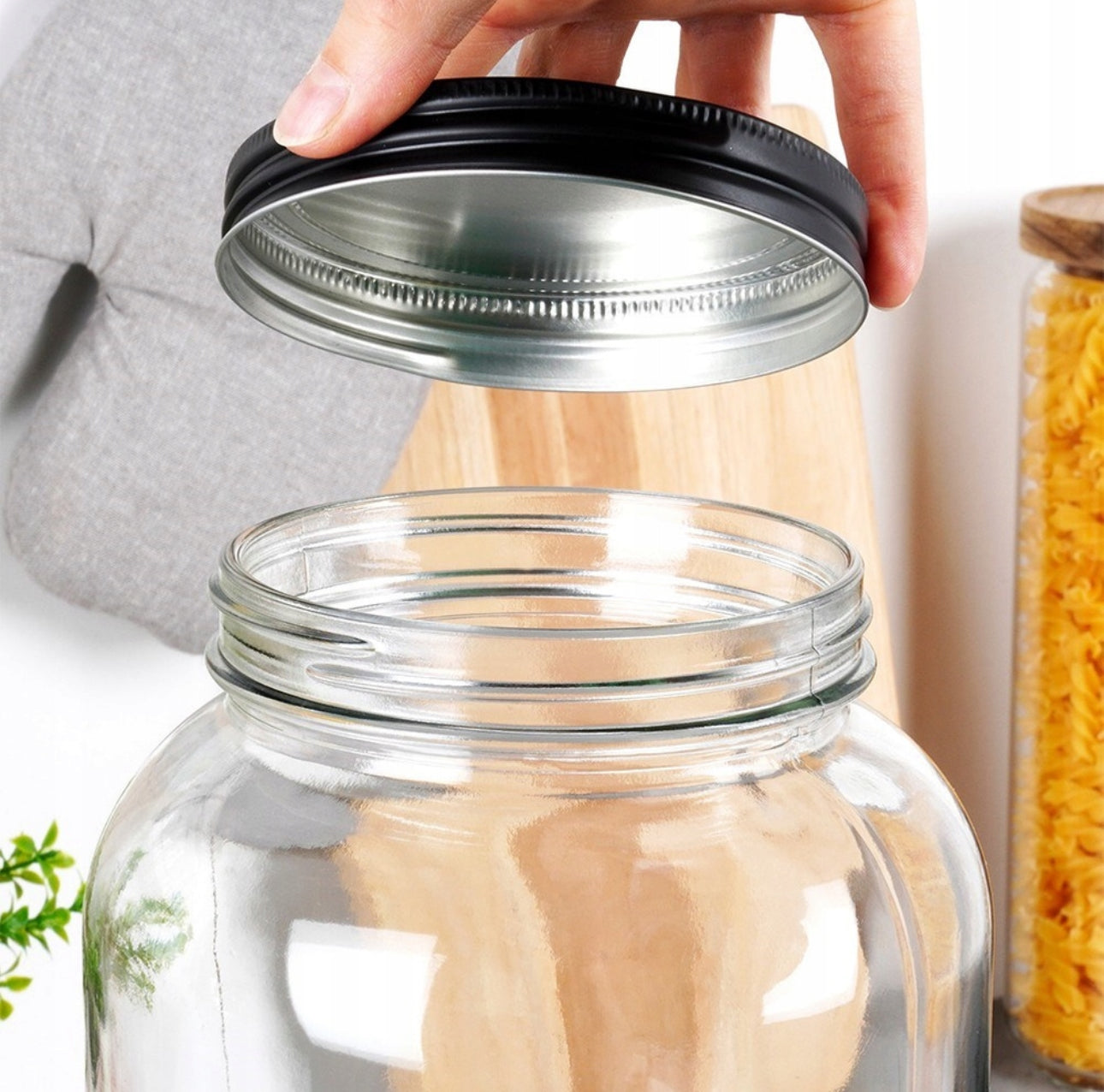 Åpen glassdispenser med hånd som holder sort metallokk over åpningen