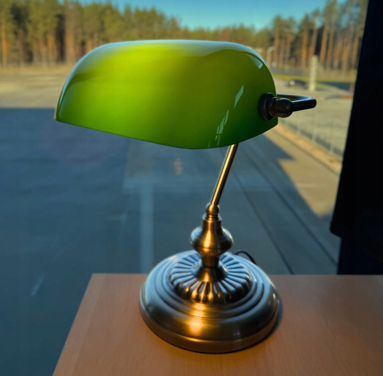Banklampe med grønn glasskjerm plassert på trebord ved vindu