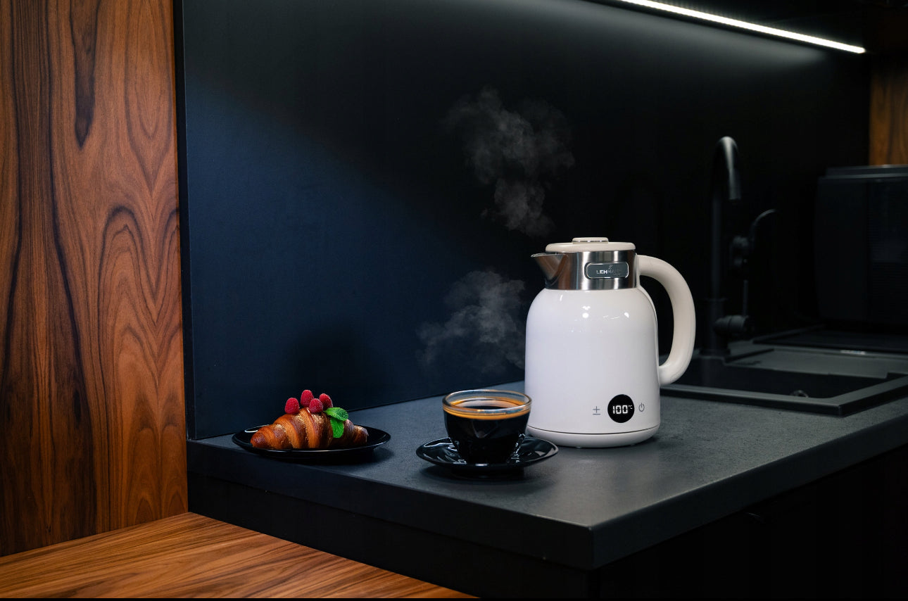Moderne vannkoker i hvit og stål på kjøkkenbenk med damp og kaffekopp ved siden