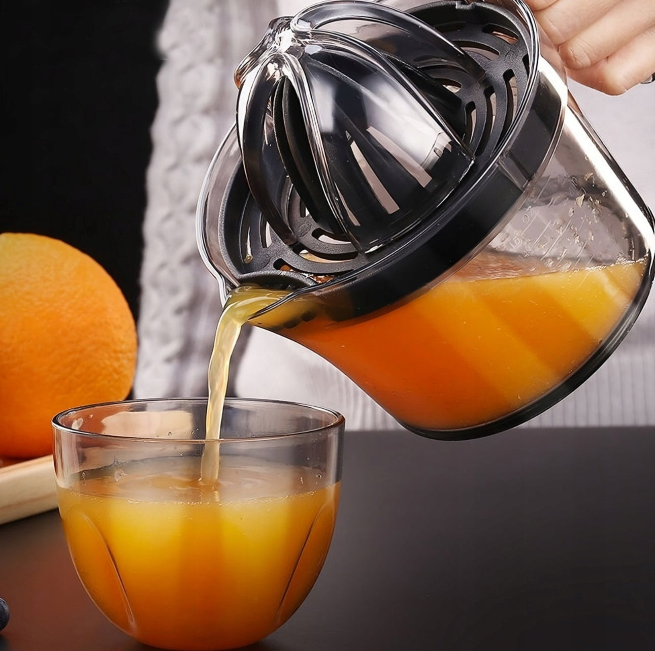 Nærbilde av appelsinjuice som helles fra sitruspresse i et glass, omgitt av appelsin og blåbær.